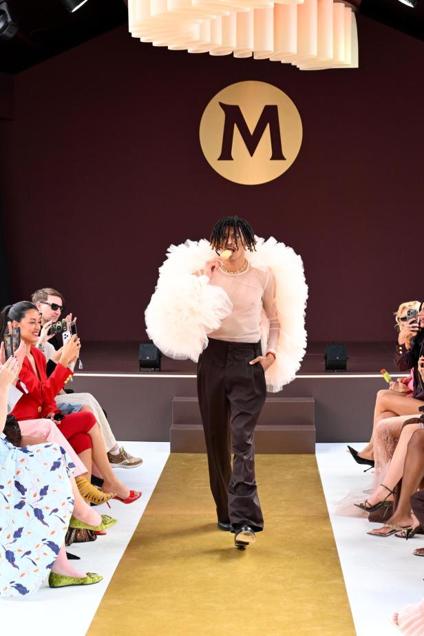 Henry Klum läuft bei der Magnum-Fashionshow in Cannes in einem auffälligen Outfit über den Laufsteg und genießt dabei ein Eis, während das Publikum Fotos macht.