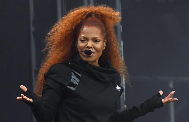 Janet Jackson mit Mikrofon und hochgesteckten, roten Haaren in einem schwarzen Oberteil.