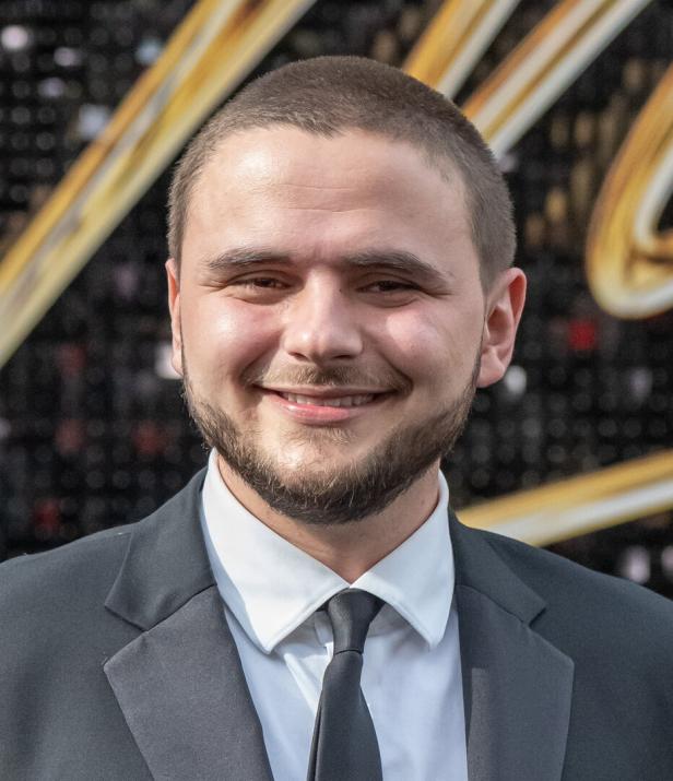 Ein lächelnder Prince Jackson mit Bart und Anzug steht vor einem goldenen Hintergrund.