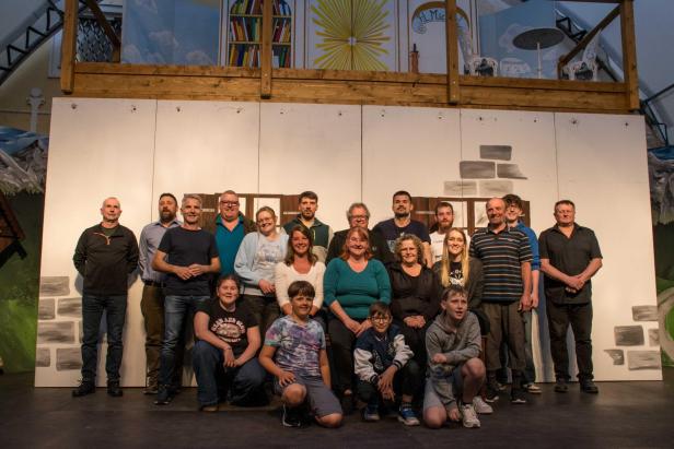Gruppenfoto der Theatergruppe vor dem Bühnenbild von „Der Brandner Kaspar und das ewige Leben“.
