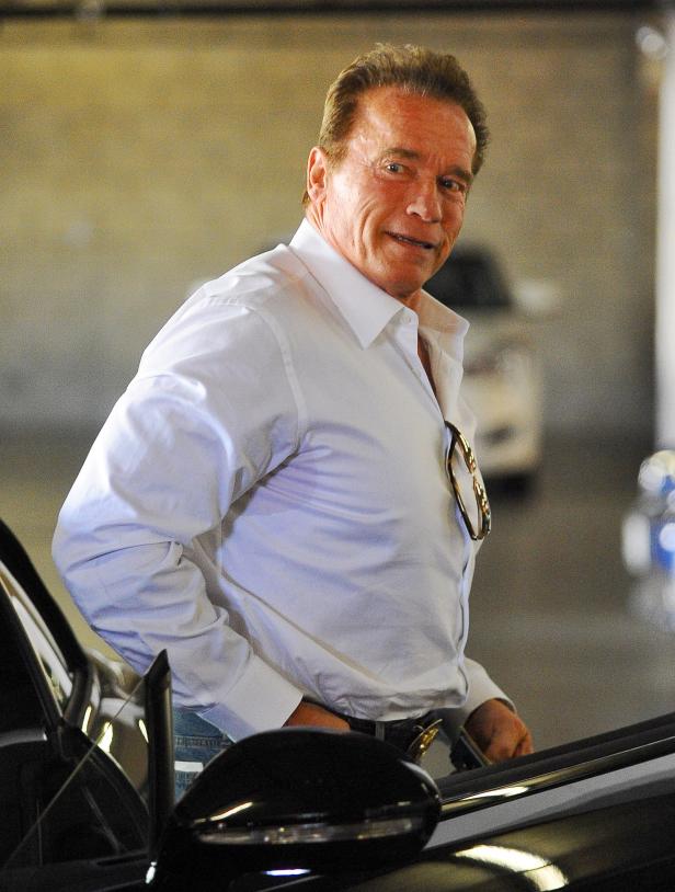 Arnold Schwarzenegger in einem weißen Hemd steht neben einem Auto.