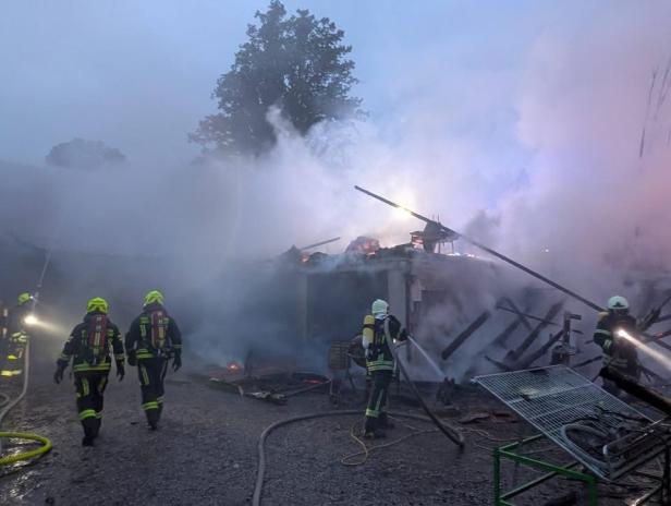 Feuerwehrleute bekämpfen einen Großbrand in einer stark verrauchten Maschinenhalle.