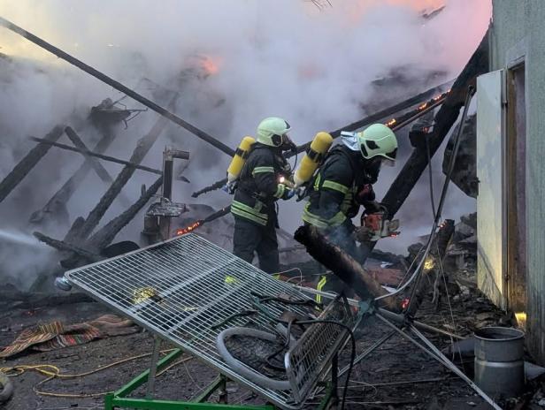 Feuerwehrleute bekämpfen einen Großbrand in einer stark verrauchten Maschinenhalle.