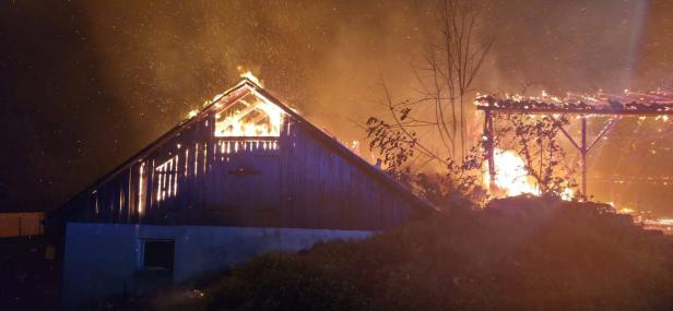 Feuerwehrleute bekämpfen einen Großbrand in einer stark verrauchten Maschinenhalle.