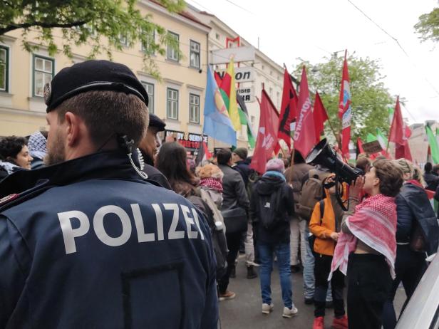 Eine Menschenmenge mit Fahnen demonstriert auf der Straße, während ein Polizist im Vordergrund steht.