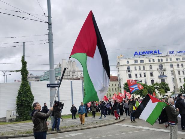 Menschen versammeln sich auf einer Straße und schwenken große palästinensische Fahnen sowie andere rote Fahnen.