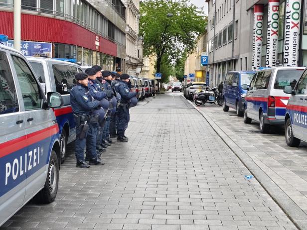 Mehrere Polizisten in Uniform stehen nebeneinander auf einer gepflasterten Straße zwischen Polizeifahrzeugen.