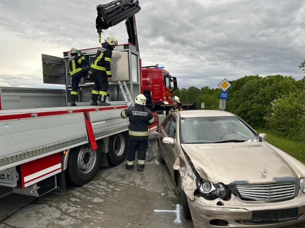 Mehrere Feuerwehrleute sichern ein beschädigtes Auto neben einem Einsatzfahrzeug auf einer Landstraße.