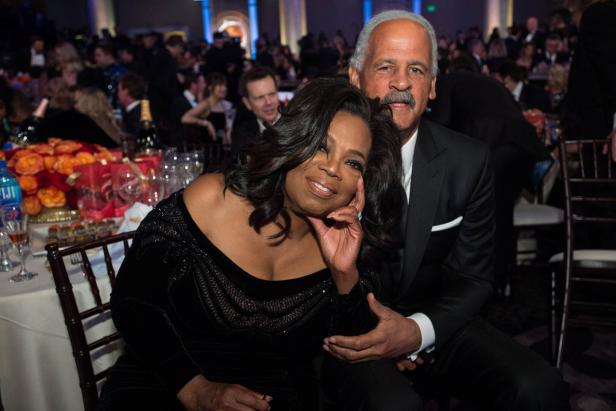 Oprah Winfrey sitzt mit einem Mann im Anzug bei einer Veranstaltung.