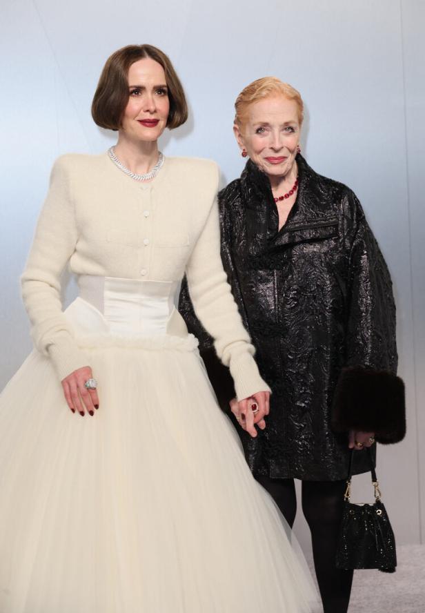 Zwei elegant gekleidete Frauen stehen nebeneinander und halten sich an den Händen.