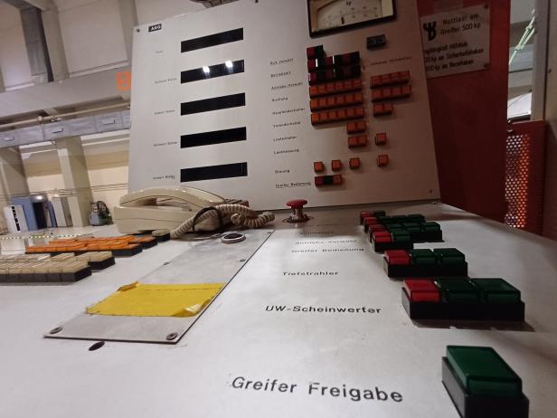 Bedienpult mit zahlreichen farbigen Tasten, einem Telefonhörer und Beschriftungen für verschiedene Steuerfunktionen.