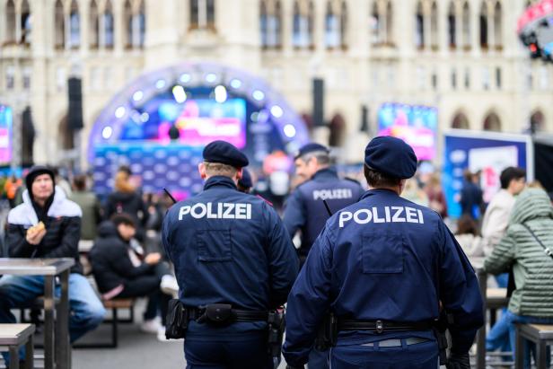 Mehrere Polizisten in Uniform überwachen eine Veranstaltung im Freien mit vielen Menschen und einer beleuchteten Bühne.
