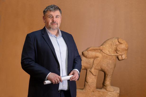 Ein Mann im Anzug steht vor einer iberischen Reiterstatue aus Stein.