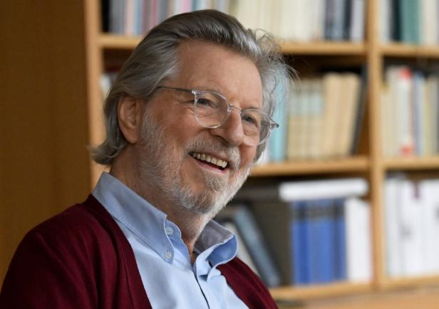 Ein älterer Mann mit Brille lächelt vor einem Bücherregal.