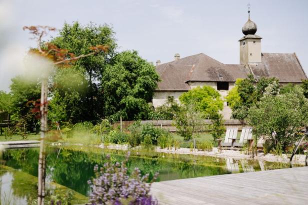 Historisches Gebäude mit Turm, Naturbadeteich und Liegestühlen im grünen Garten.