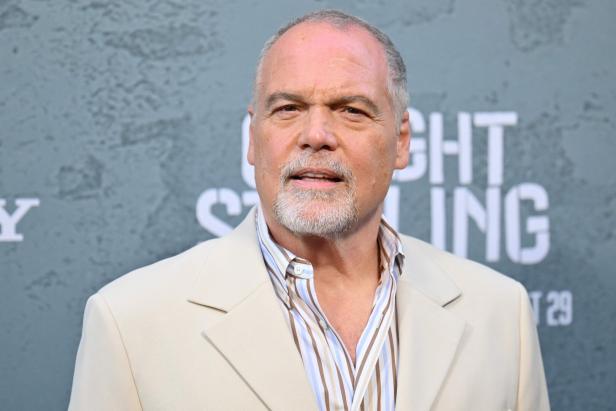 Vincent D'Onofrio mit grauem Bart und kurzem Haar trägt ein cremefarbenes Sakko und ein gestreiftes Hemd vor grauem Hintergrund.