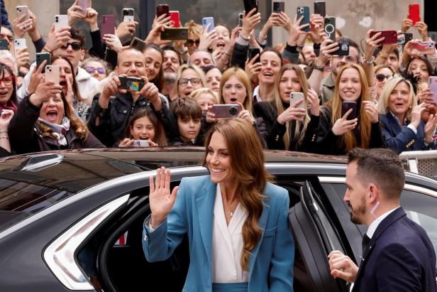 Kate winkt lächelnd aus einem Auto, während eine Menschenmenge Fotos macht.