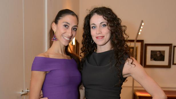 Zwei Frauen posieren in eleganten Kleidern für ein Foto.
