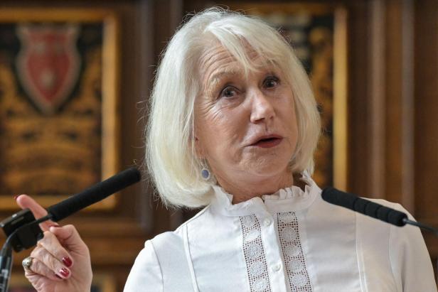 Helen Mirren mit weißem Haar spricht vor Mikrofonen und trägt eine weiße Bluse.