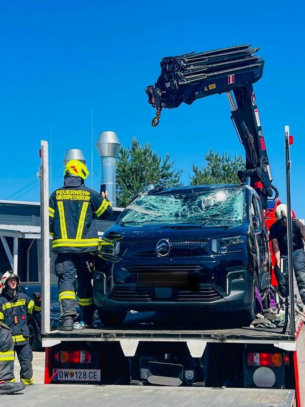 Feuerwehrleute bergen ein Auto mit stark beschädigter Windschutzscheibe von einem Abschleppfahrzeug mit Kran.