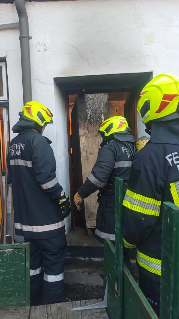 Drei Feuerwehrleute in Schutzkleidung und Helmen entfernen einen verbrannten Gegenstand aus einem Gebäude.