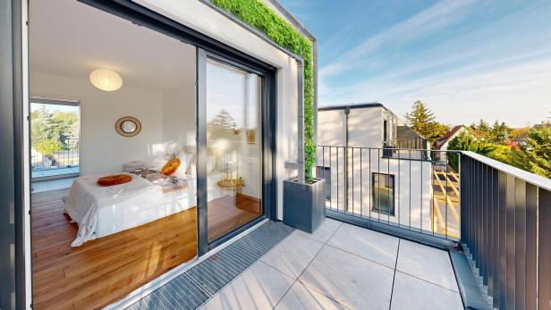Ein Balkon grenzt an ein lichtdurchflutetes Schlafzimmer mit Holzelementen 