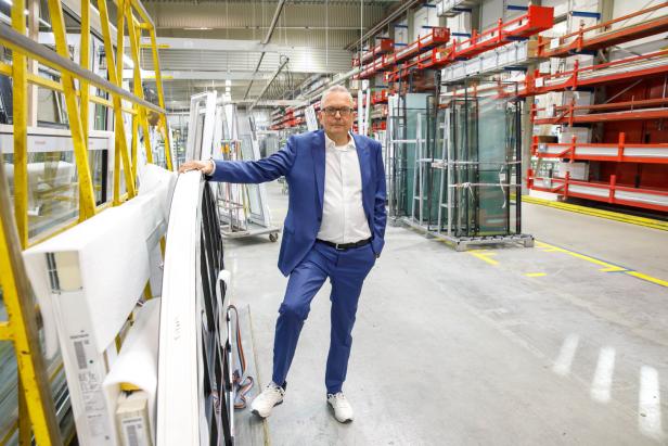 Ein Mann im blauen Anzug steht in einer modernen Fabrikhalle zwischen Glas- und Fensterrahmen.