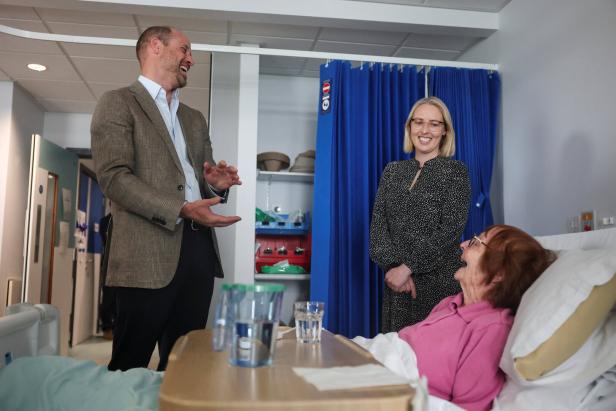 Prinz William im Sakko und eine Frau besuchen eine Patientin im Krankenhaus.