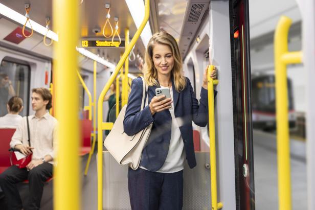 Frau in Businesskleidung steht in einer U-Bahn und nutzt ihr Smartphone.
