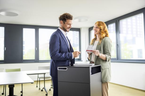 Zwei Personen unterhalten sich lächelnd in einem modernen Büro und halten ein Dokument.