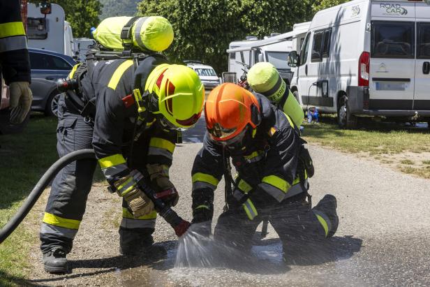 Zwei Feuerwehrleute in Schutzkleidung spritzen Wasser aus einem Schlauch auf den Boden zwischen Wohnmobilen.