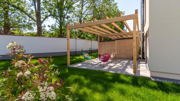 Moderne Terrasse mit Holzpergola, bunten Stühlen und Garten im Grünen bei Sonnenschein.
