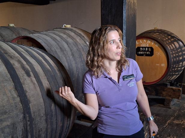 Eine Frau von Blandy's Madeira steht vor großen Weinfässern und erklärt etwas.