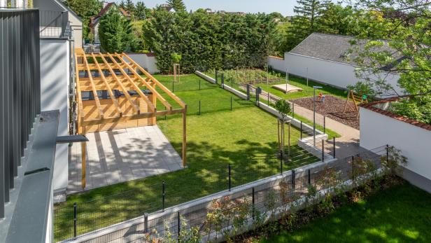 Ein grüner Garten. Darüber eine Pergola aus Holz 