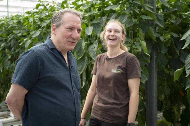 Robert Palfrader und Lisa Thell stehen lachend zwischen Paprikapflanzen im Gewächshaus des Gemüsebetriebs Thell im Seewinkel.