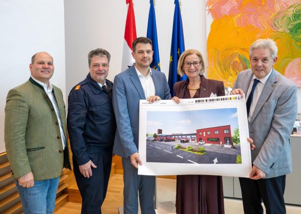 Fünf Personen stehen zusammen und halten eine Visualisierung eines modernen roten Gebäudes mit Parkplatz.