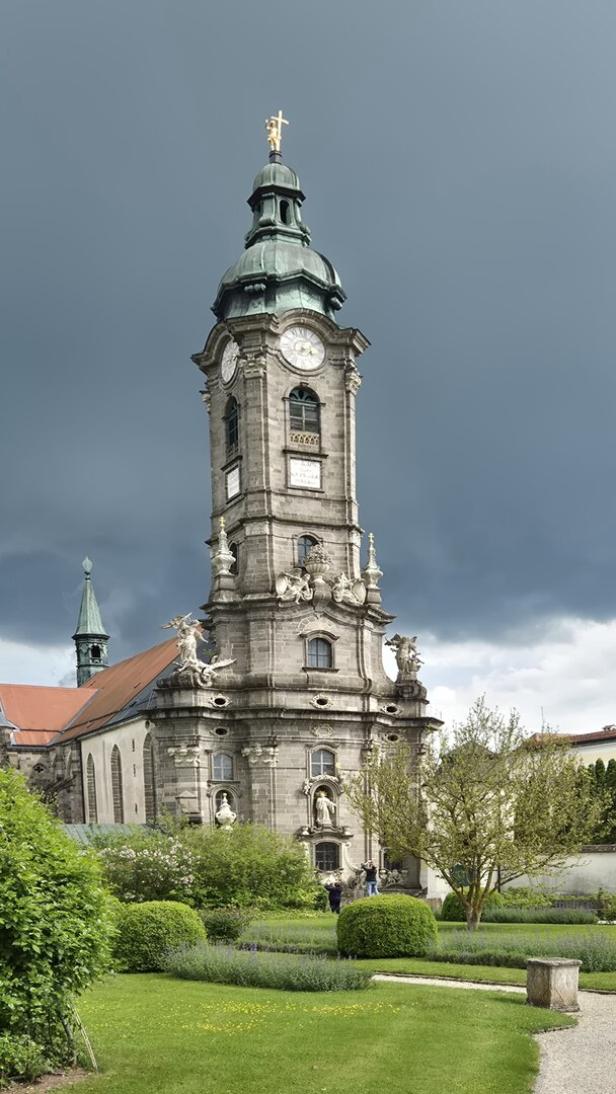 Ein Kirchturm mit Uhr und grüner Spitze ragt vor einem dunklen Himmel empor.