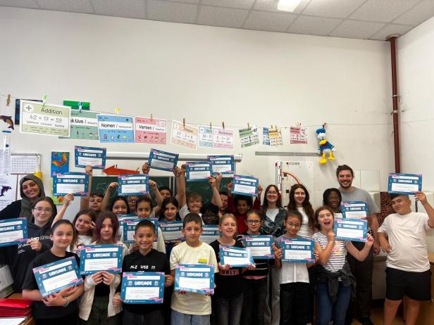 Eine Schulklasse hält stolz ihre Changemaker Markttag Urkunden in die Höhe. Sie sind in einer Schulklasse.