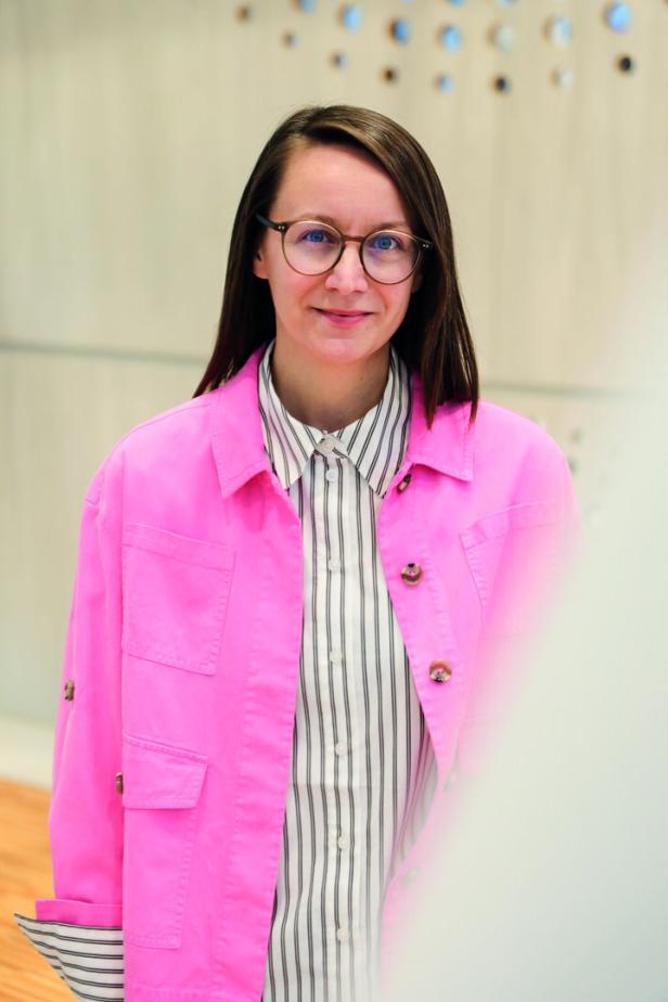 Eine Frau mit Brille und rosa Jacke lächelt in die Kamera.