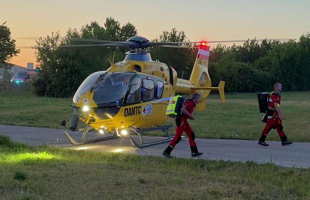Rettungshubschrauber mit zwei Notfallsanitätern auf einer Wiese bei Sonnenuntergang.