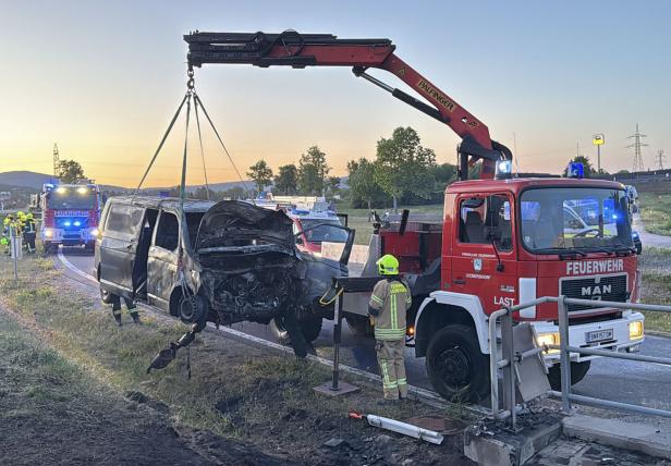 Ein ausgebrannter Transporter wird von einem Feuerwehrkran geborgen, Einsatzkräfte vor Ort.