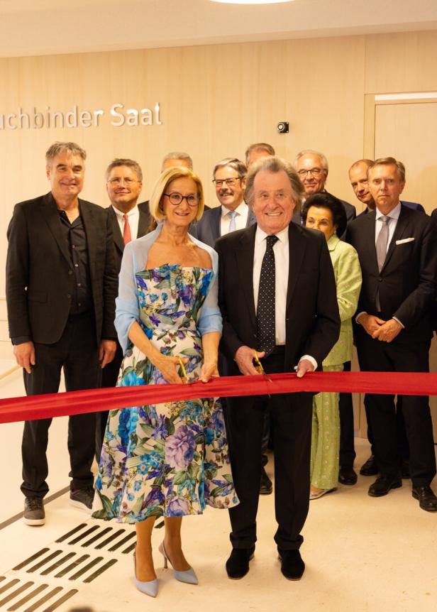 Mehrere elegant gekleidete Personen durchschneiden gemeinsam ein rotes Band bei einer feierlichen Eröffnung.