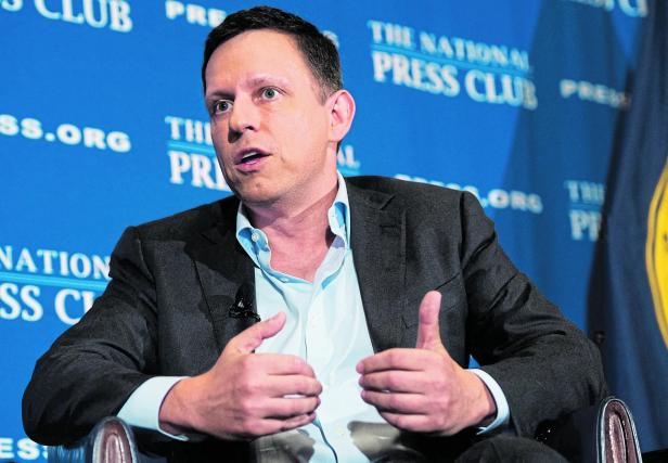 Ein Mann im Anzug spricht gestikulierend vor einer blauen Wand mit der Aufschrift „The National Press Club“.