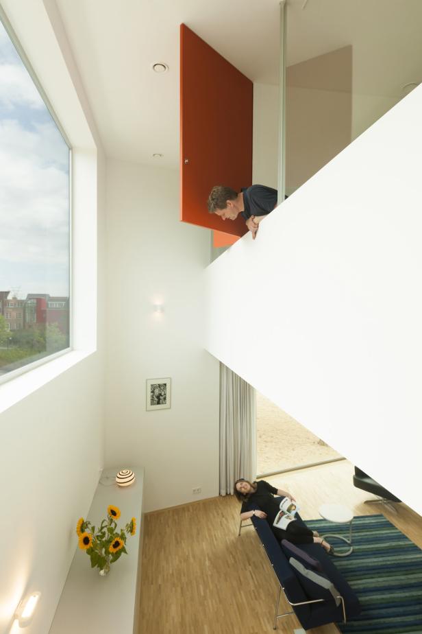 1. Platz: Entwurf Stripe House in Leiden (NL) von Gaaga Studio for Architecture. Ein Mann schaut von einer Galerie auf eine Frau, die auf einer Couch liegt.