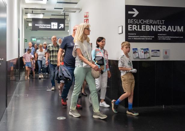 Mehrere Menschen gehen durch einen Flur in Richtung einer Besucherterrasse, darunter Erwachsene und Kinder.