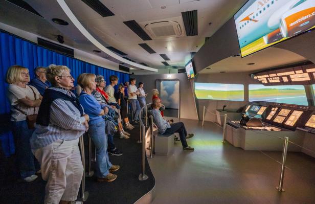 Mehrere Menschen beobachten aufmerksam eine Simulation in einem Raum mit Cockpit-Attrappe und Bildschirmen.