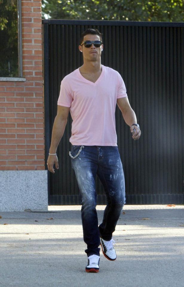 Cristiano Ronaldo mit Sonnenbrille trägt ein rosa T-Shirt, blaue Jeans und weiße Turnschuhe und geht draußen entlang.