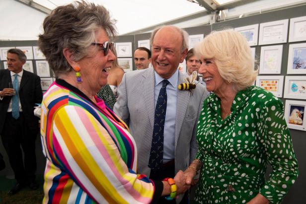 Königin Camilla trifft Prue Leith in bunter Jacke, während ein Mann mit Bienen-Anstecker lächelt.