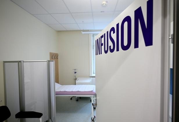 Ein Behandlungsraum mit Liege, Infusionsständer, Trennwand und geöffneter Tür mit der Aufschrift „INFUSION“.