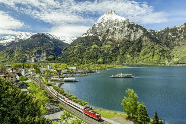 Der Gotthard Panorama Express vor einem See und einer Berglandschaft. 